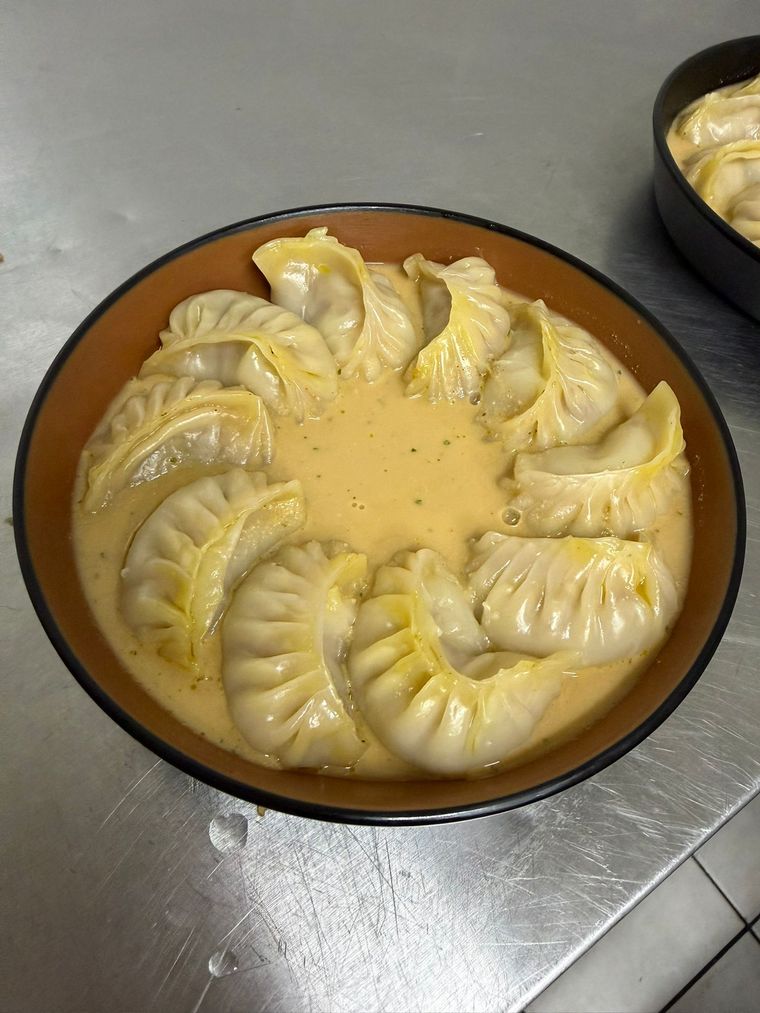 A bowl of steamed momo sitting in creamy sesame jhol sauce