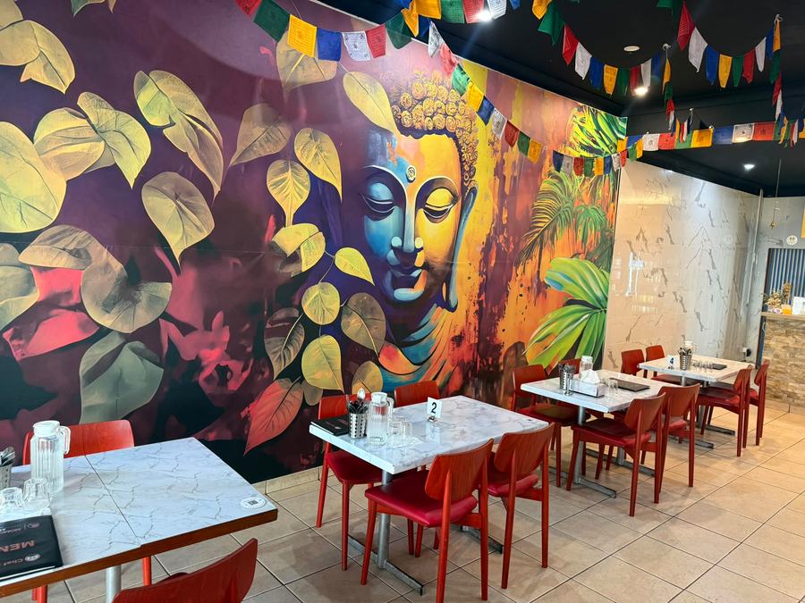 Marble tables and red chairs beneath the mural and prayer flags